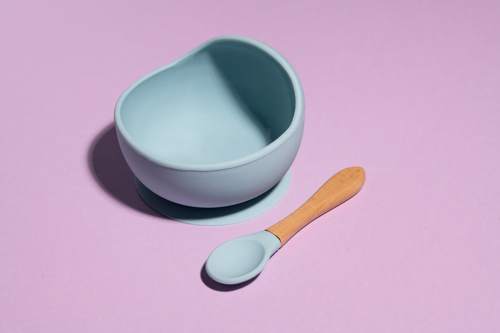 Otroška silikonska skleda z žličko, ki se prisesa na mizo v vijolični ali modri barvi. Enostavna za čiščenje.