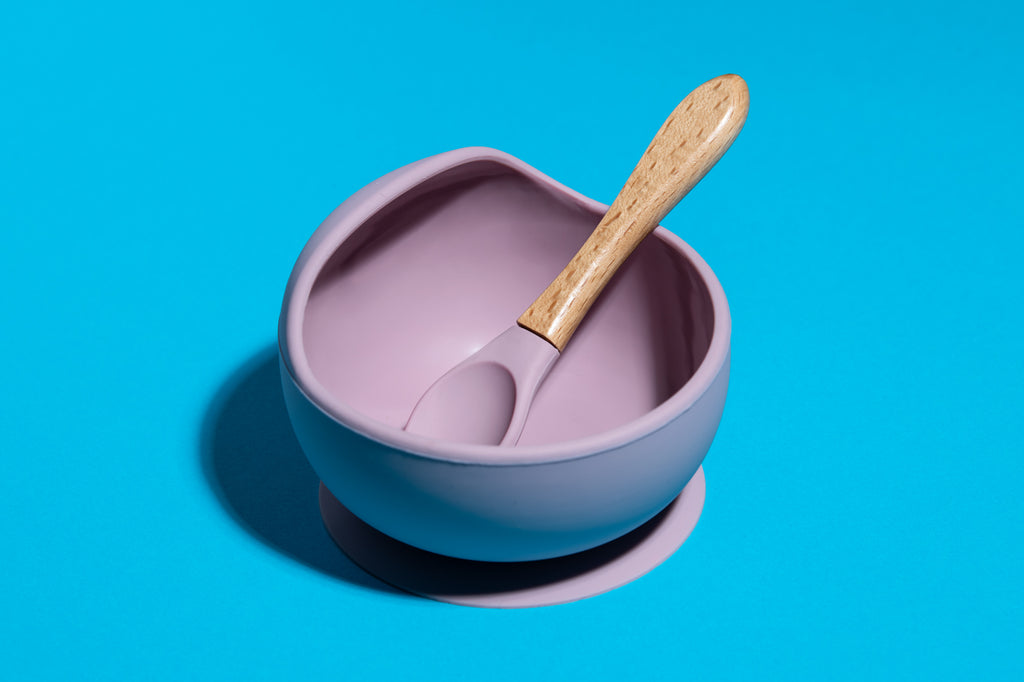 Otroška silikonska skleda z žličko, ki se prisesa na mizo v vijolični ali modri barvi. Enostavna za čiščenje.